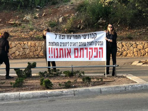 אישה מחזיקה שלט בהפגנת אלמנות ויתומי צה"ל