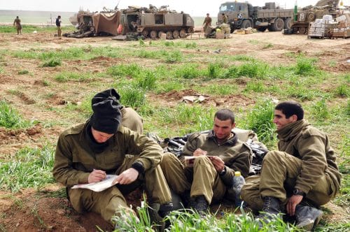 חיילים נחים וכותבים בשטח על רקע ציוד צבאי פרוס