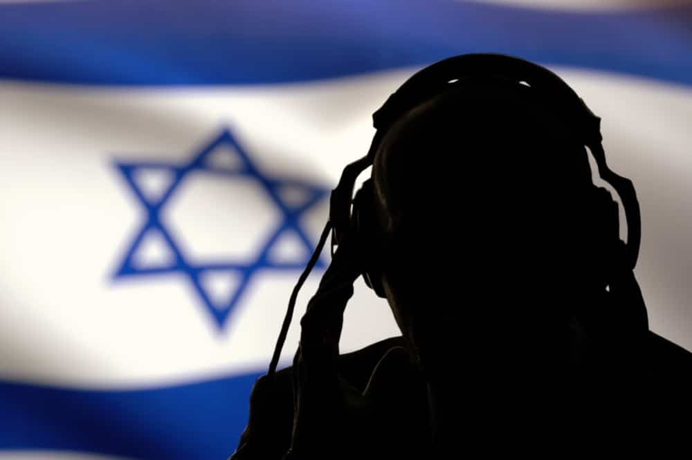 A dark figure with headphones and the Israeli flag in the background