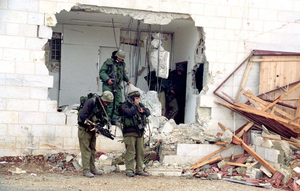 IDF soldiers standing near a large break in a house wall