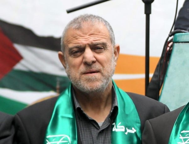 Suhail al-Hindi with a green hamas scarf and a palestinian flag in the background