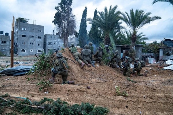 חיילי צה"ל שוכבים על דיונה בין עצי דקל מול בניינים 