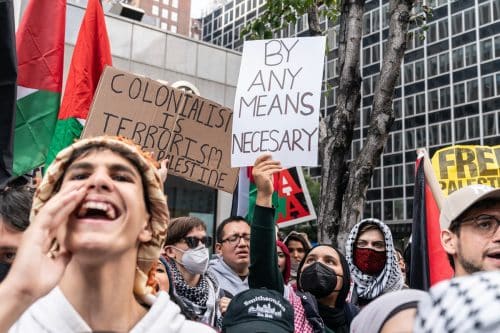 מפגינים עם כאפיות ודגלים פלסטינים אוחזים בשלטים 'בכל דרך אפשרית' ו'קולוניאליזם הוא טרור'