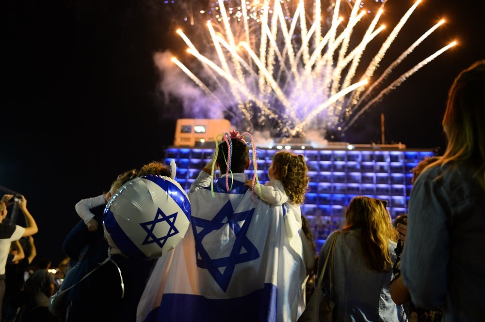 אב וילדה עטופים בדגל ישראל ומביטות בזיקוקים