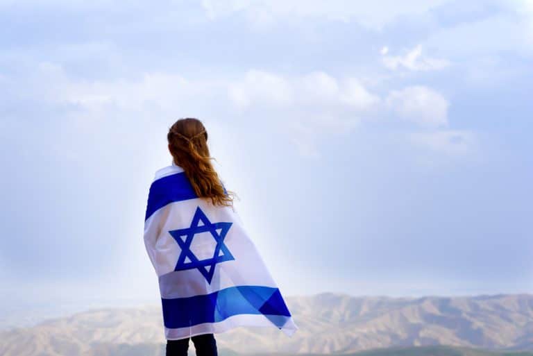 נערה עטופה בדגל ישראל מביטה לנוף