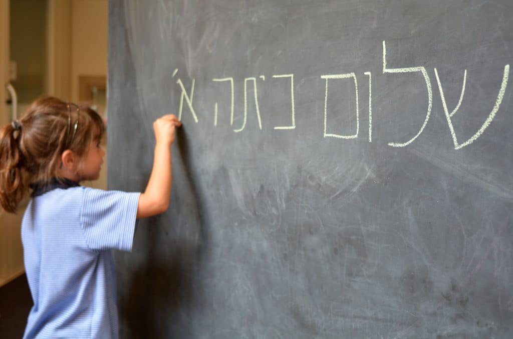 child writes with chalk on a blackboard