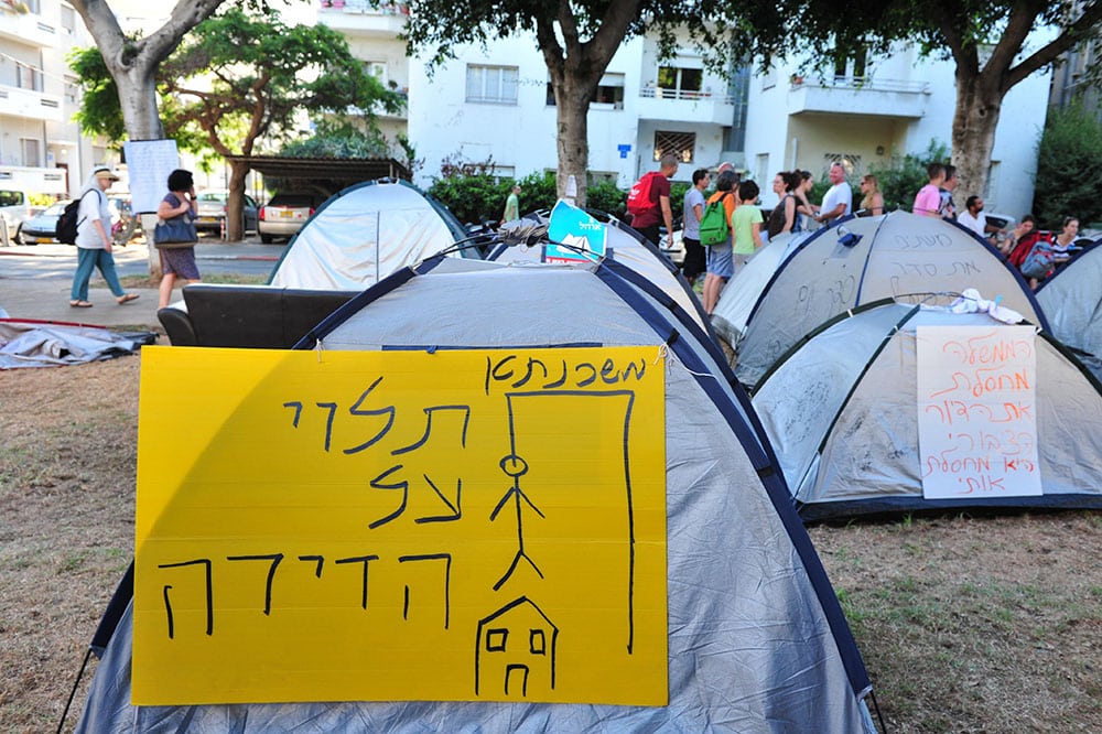 אוהלים בתל אביב ושלט 'משכנתא תלוי על הדירה' עם ציור איש תלוי מעל בית