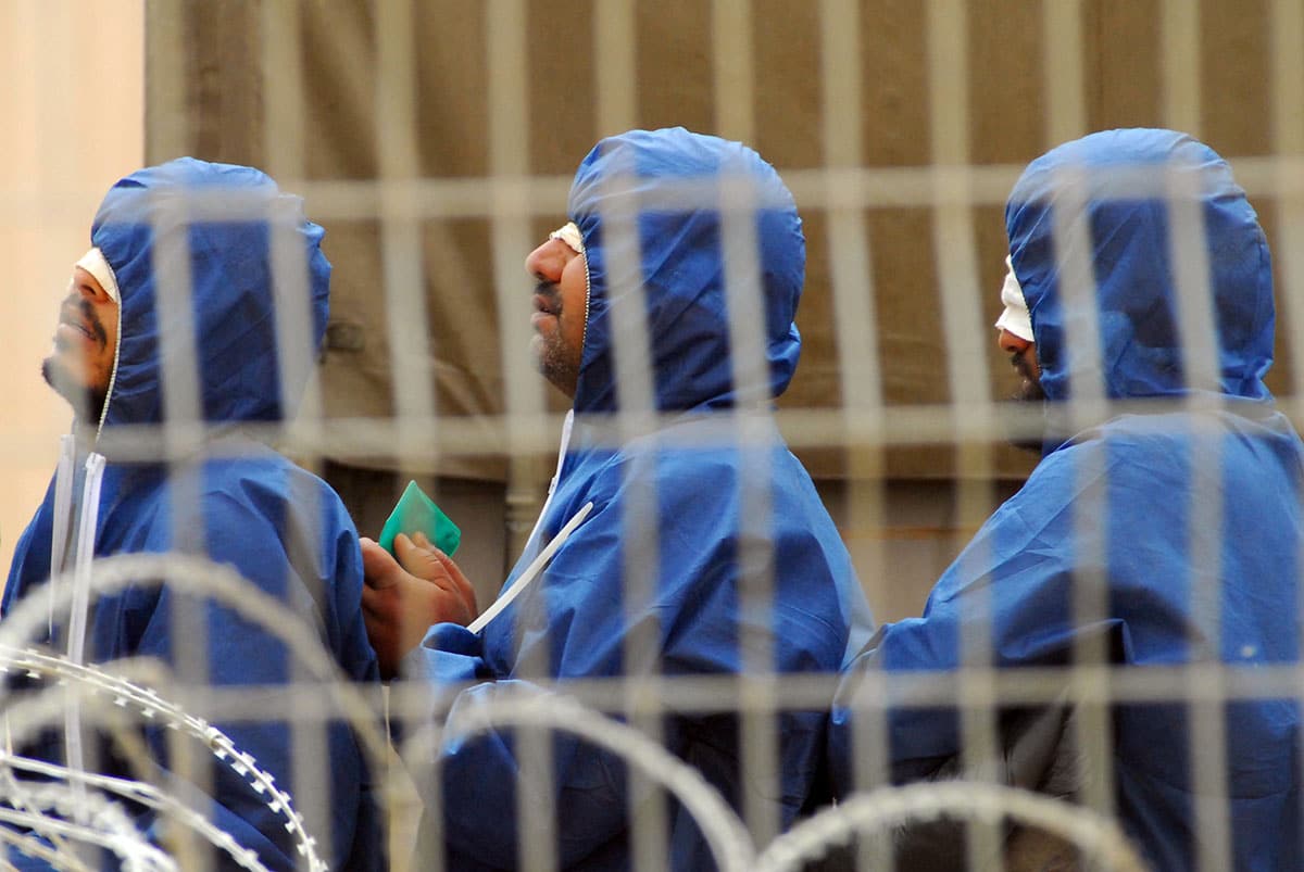 Three handcuffed blindfolded terrorists in blue clothing in prison