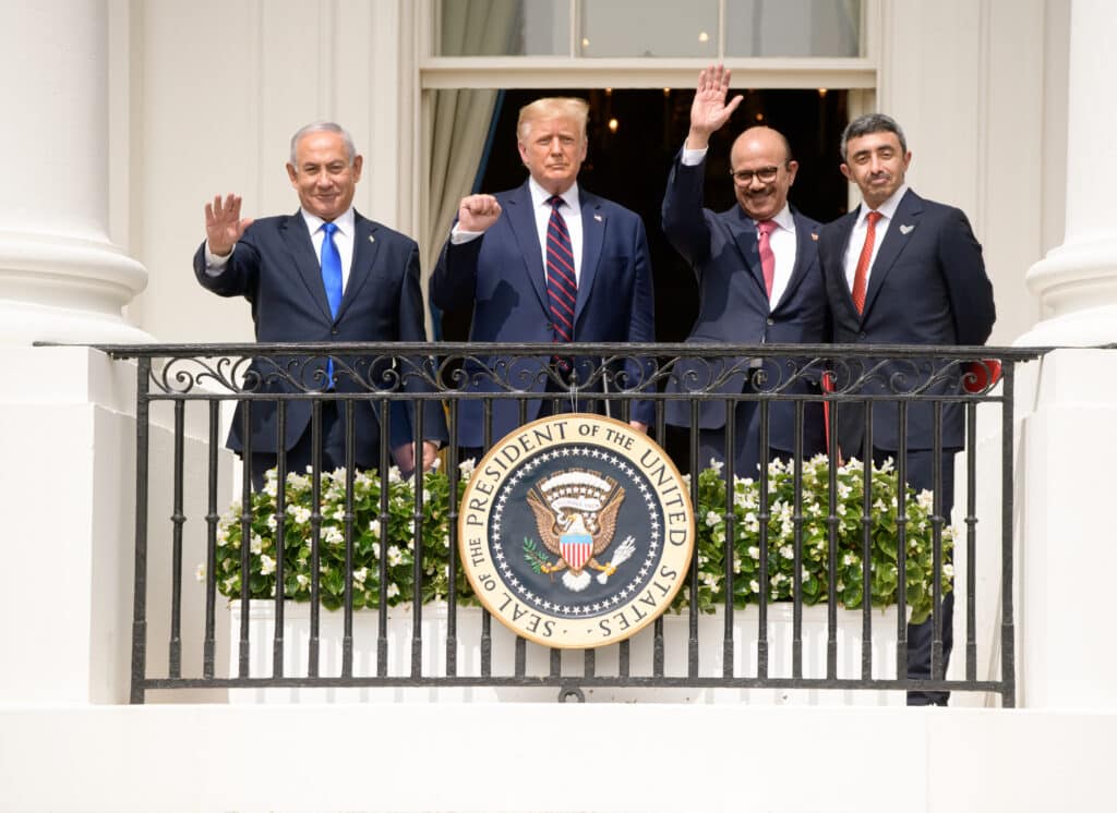ארבעה מנהיגים רשמיים עומדים על מרפסת הבית הלבן בטקס הסכמי אברהם, מנופפים לציבור מעל חותם נשיא ארצות הברית.
